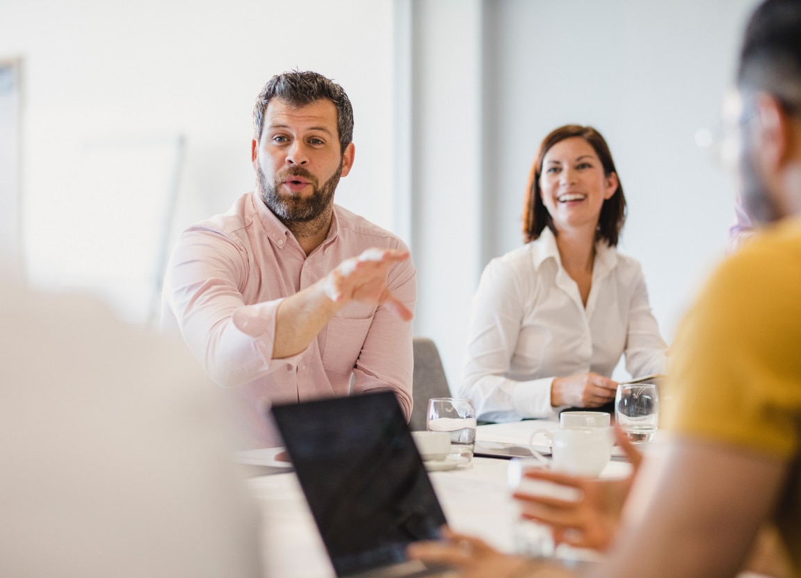 Man in light pink shirt talking to colleagues at a boardroom table